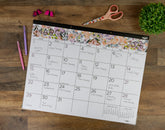 Floral March 2026 calendar on a wooden surface with stationery items.