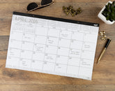 Medium desk pad Calendar for April 2026 on a wooden surface with accessories.