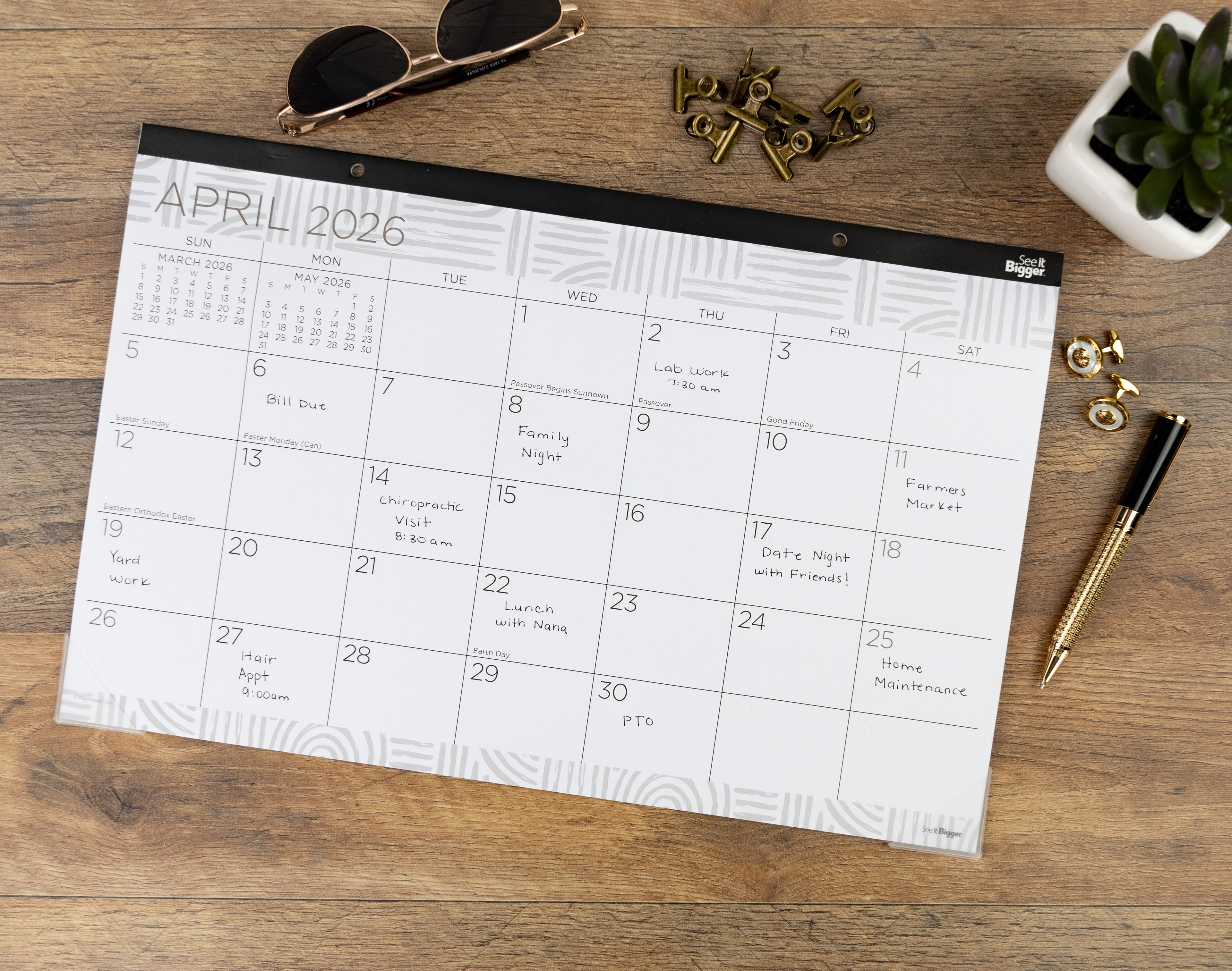 Medium desk pad Calendar for April 2026 on a wooden surface with accessories.